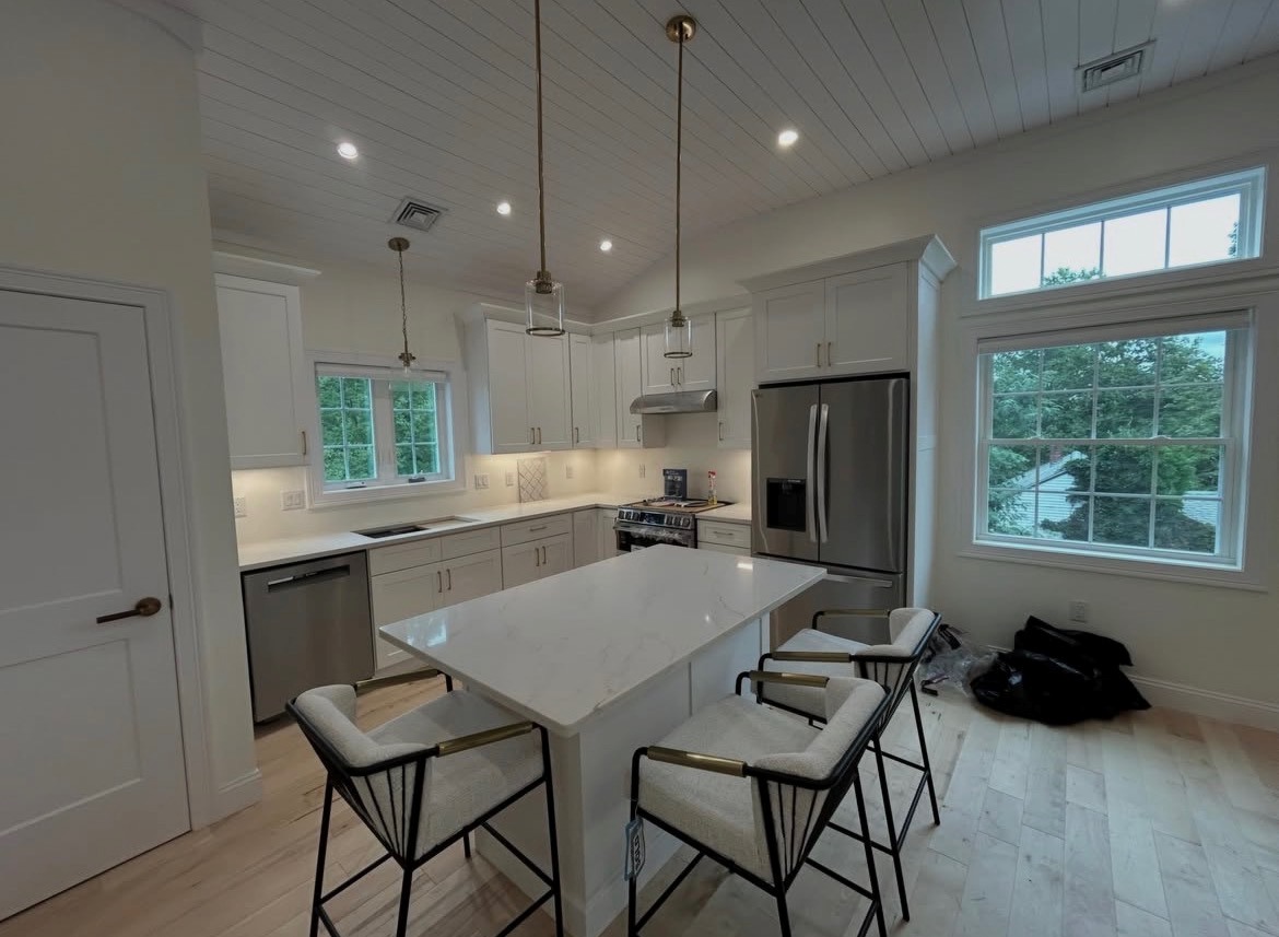 Boston Light & Power electrician installing pendant and recessed lighting over a white kitchen island in Milton, MA.